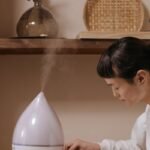 A person adjusting a aromatherapy humidifier in a cozy, minimalist interior setting.