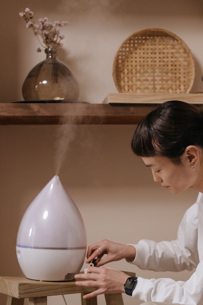 A person adjusting a aromatherapy humidifier in a cozy, minimalist interior setting.