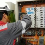 Digital Clamp Meter vs Digital Multimeter - Electrician testing voltage in an industrial breaker panel with a multimeter